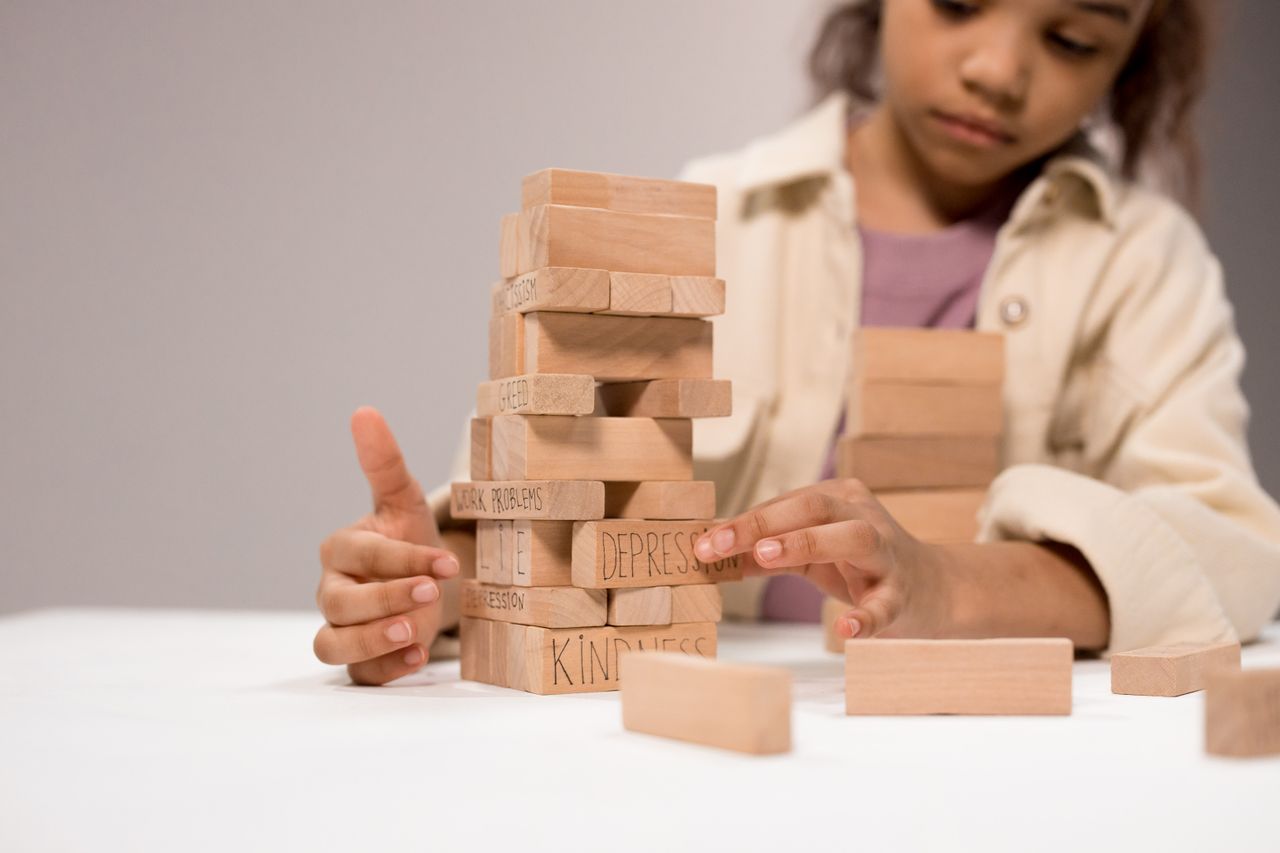 Services A child thoughtfully stacks wooden blocks with words like 'depression' and 'kindness.'